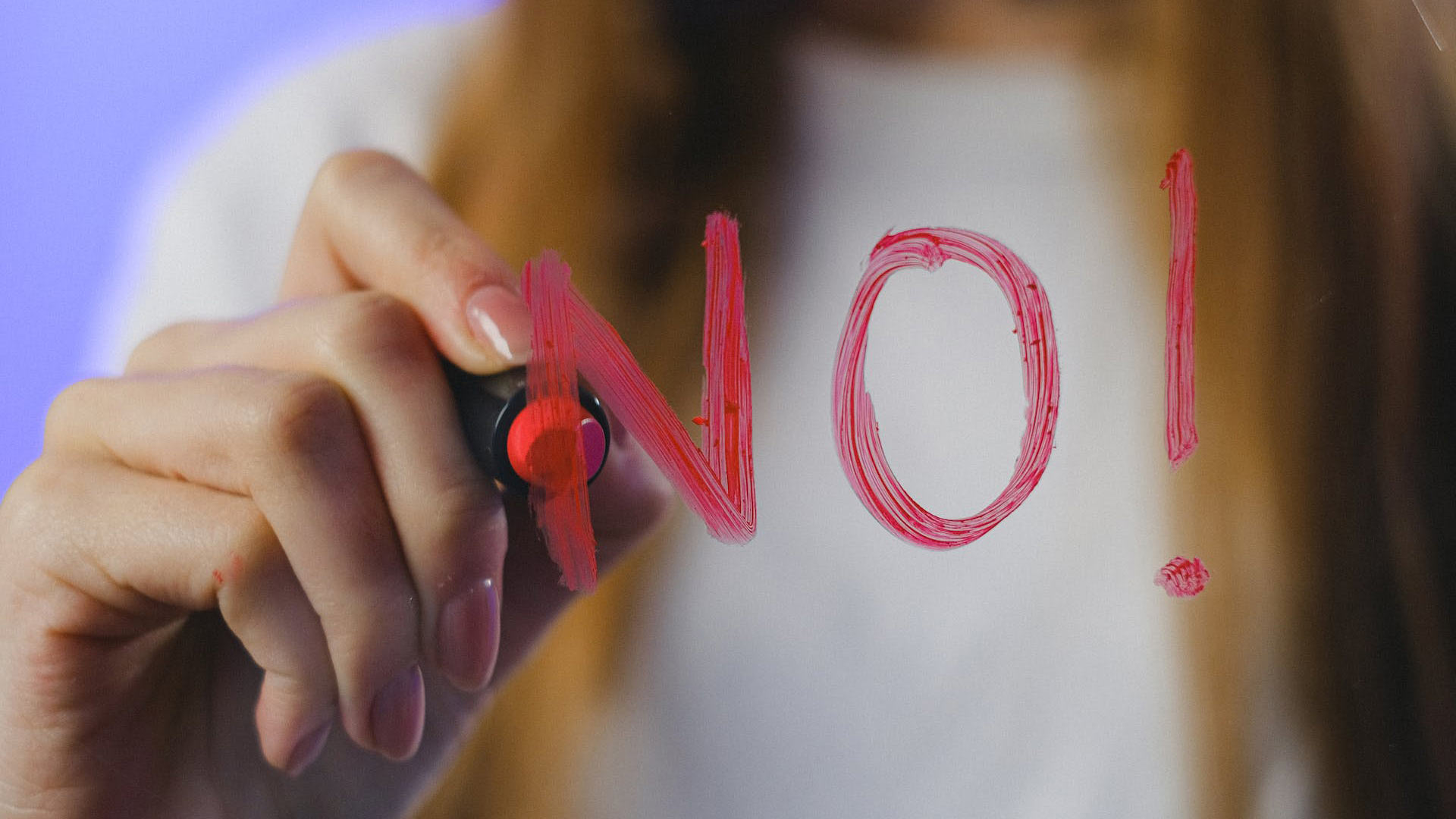 The word “NO!” Is being written on a piece of glass, using a red glass marker.
