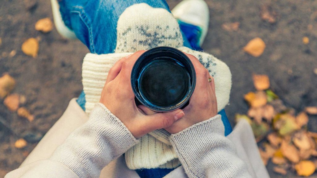 A person holds a coffee mug and rests it on a pair of mittens.