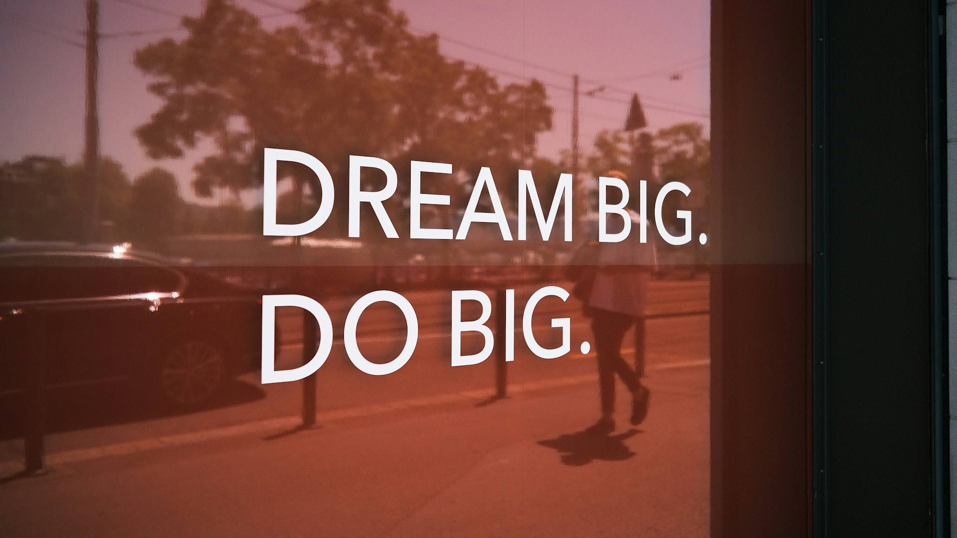 A white decal on a window says “Dream big. Do big.”