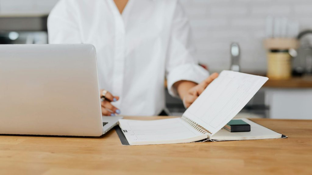 A person writes in a journal next to a laptop.