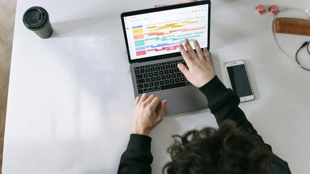 A person looks at a digital schedule with color blocks on their laptop.