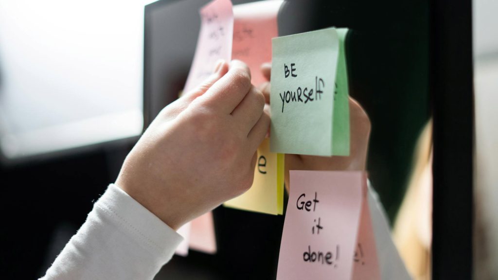 A person puts sticky notes on a mirror, each one featuring an uplifting phrase or reminder.