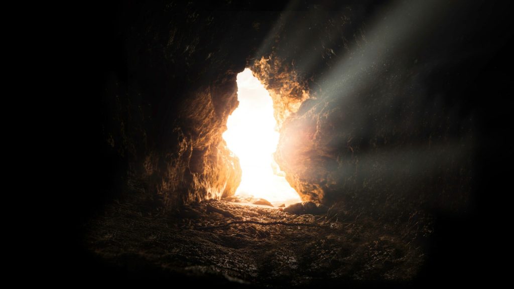 Light shines throught he entrance of a dark cave.